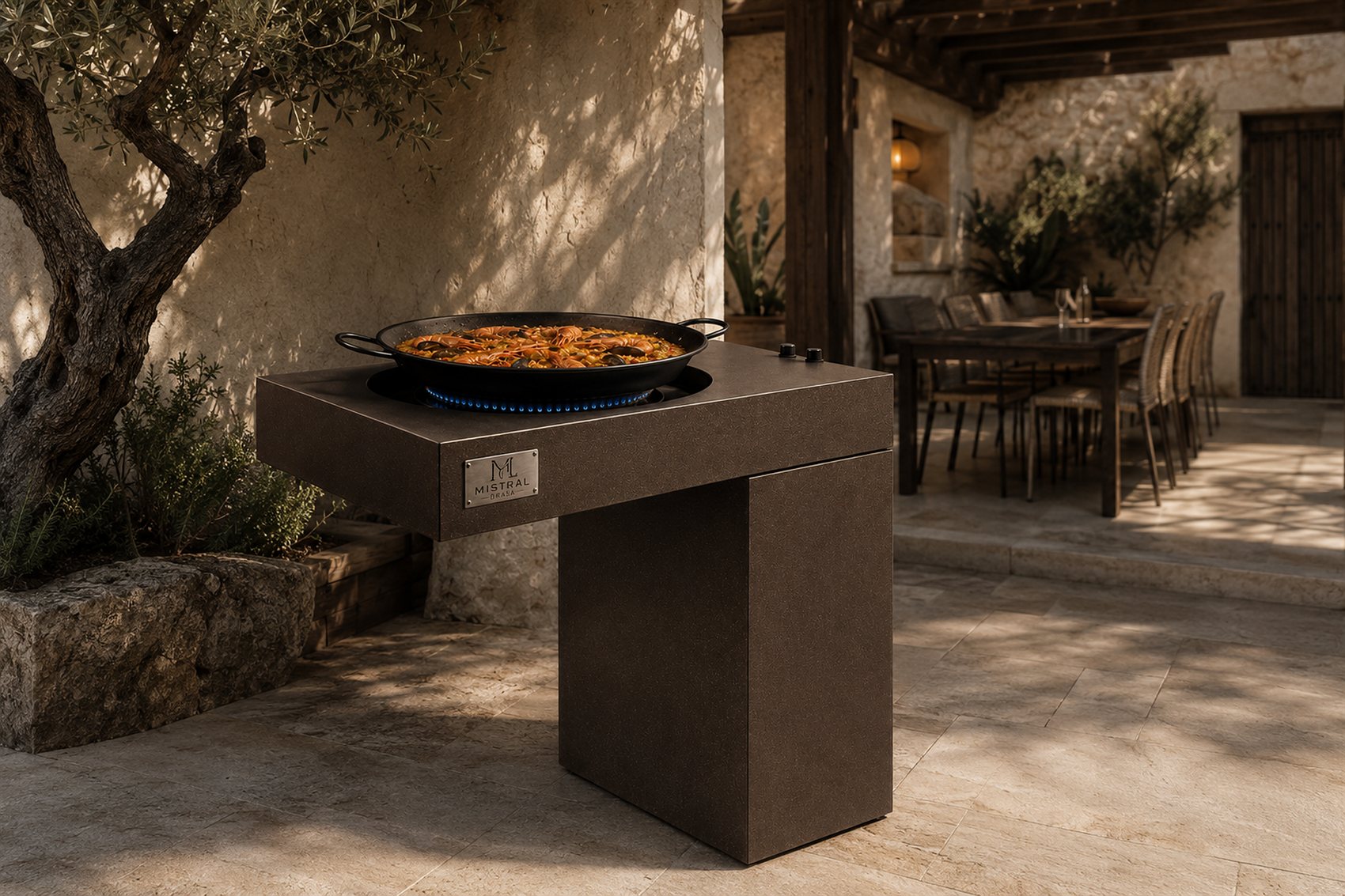 Paella sobre una pieza Mistral Brasa en un patio mediterráneo entre olivos